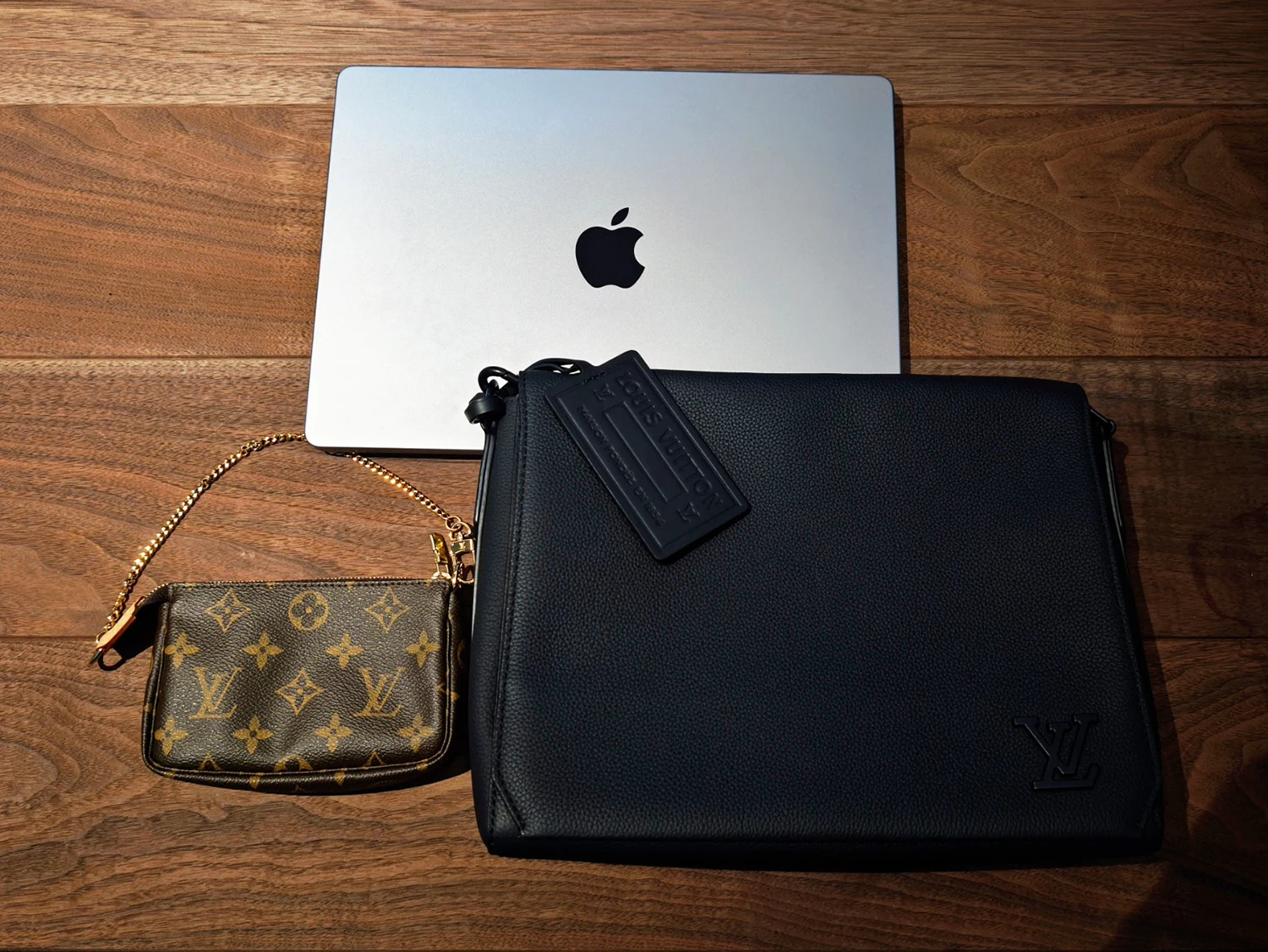 木の天板に置かれたMacBook、黒いバッグ、モノグラム柄のバッグ。